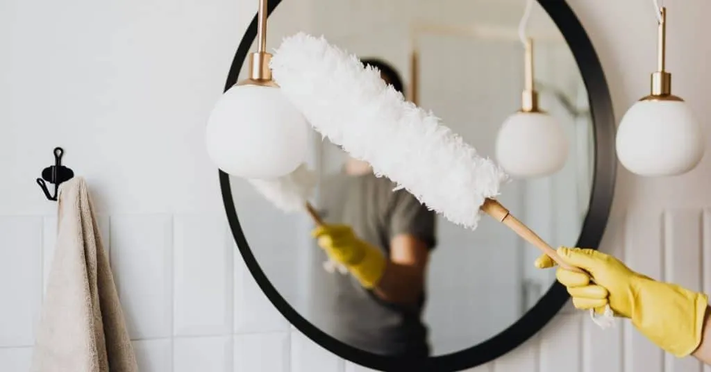 Cleaner holding a microfibre hand duster towards a mirror