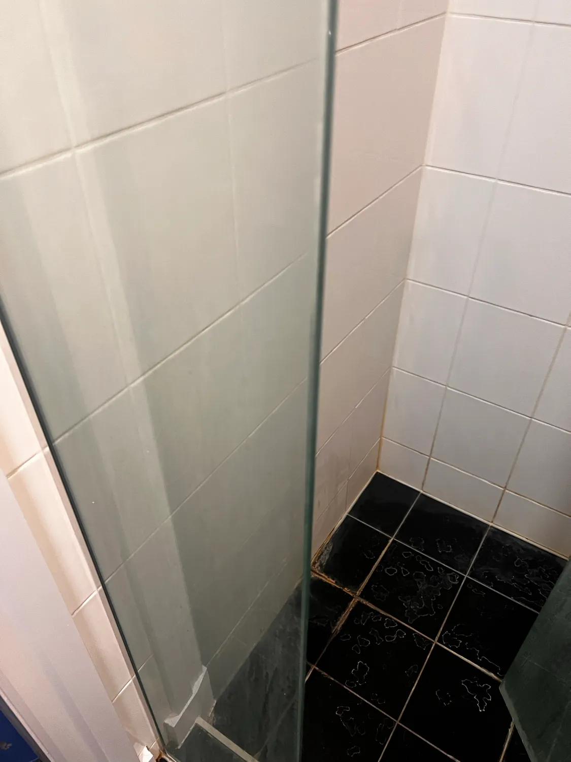 Shower glass with black tiles before cleaning